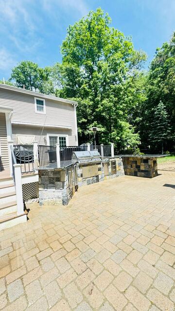 Wide view of paver patio with outdoor kitchen along deck stairs